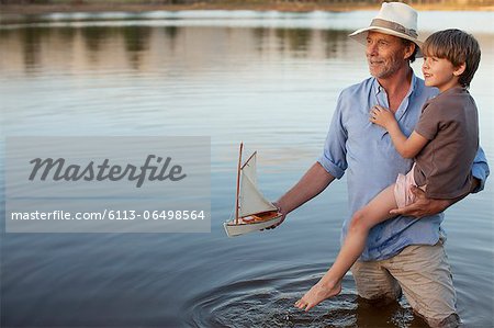 Grandfather and grandson with toy sailboat in lake