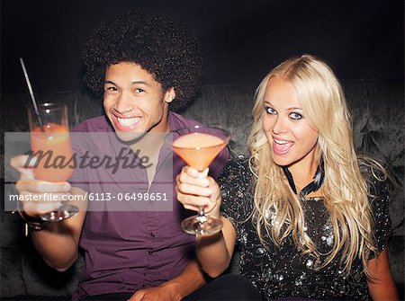 Portrait of enthusiastic couple toasting cocktails in nightclub