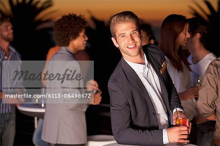 Portrait of smiling man with cocktail on balcony at sunset
