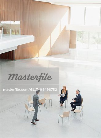 Businessman approaching co-workers at circle of chairs