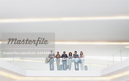 Portrait of business people standing at glass balcony railing in modern office