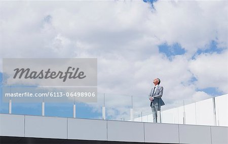 Pensive businessman looking up at sky on rooftop balcony