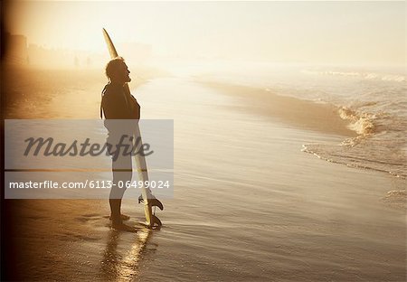 Surfer standing with board on beach