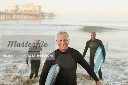 Older surfers carrying boards on beach