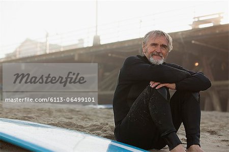 Older surfer sitting with board on beach