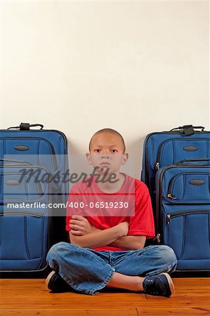 A boy sitting in front of suitcases appears upset.