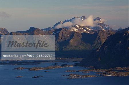 Scenic mountain peaks on Lofoten islands in Norway covered in scattered clouds with small fishing villages on the coast and rocky islands in the sea