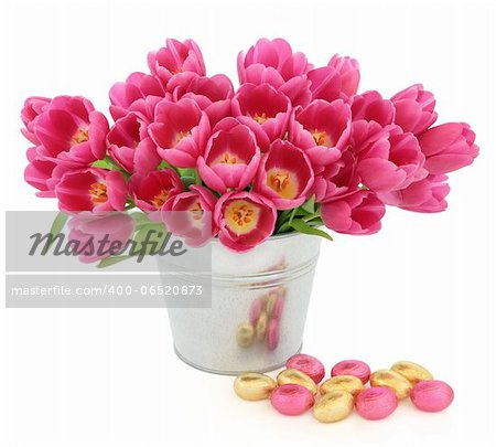 Easter egg group with pink tulip flowers in a metal vase over white background.