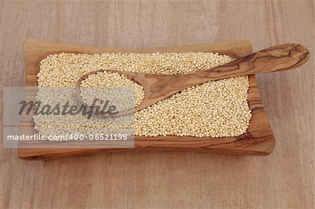 Quinoa grain in an olive wood bowl and spoon over papyrus background.