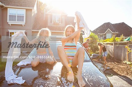 A family washes their car in the driveway of their home on a sunny summer afternoon in Portland, Oregon, USA