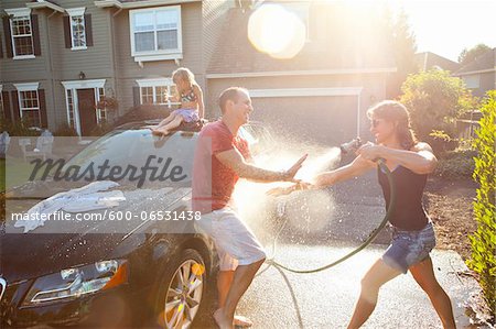 A family washes their car in the driveway of their home on a sunny summer afternoon in Portland, Oregon, USA