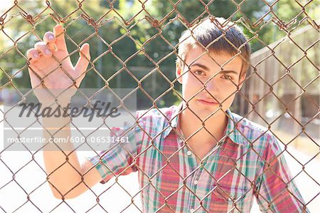 Portrait of young man standing behind chain link fence in park near the tennis court on a warm summer day in Portland, Oregon, USA