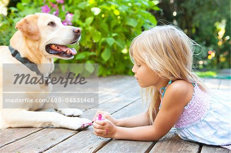 Little girl painting the claws of a dog with bright pink nail polish on a sunny summer afternoon in Portland, Oregon, USA