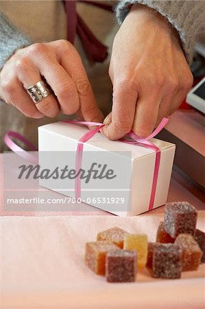 Close-Up of Woman's Hands Tying Bow on Small White Gift Box in Shop, with Candies in Foreground, Paris, France