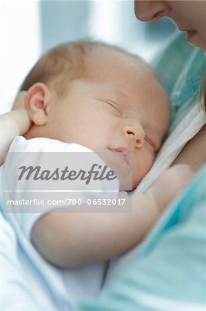 newborn baby girl in a white undershirt sleeping in the arms of mother wearing a blue shirt