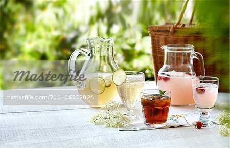 Three summer cordial beverages with mint, lime, and strawberry in an outdoor setting