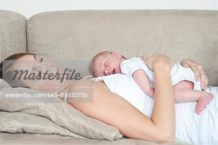 Mother sleeping with infant son on sofa