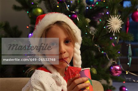 Girl wearing Santa hat by Christmas tree