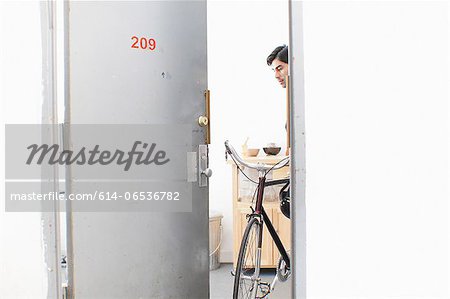 Man wheeling bicycle out apartment door