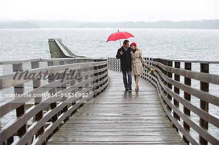 Couple walking on wooden pier in rain