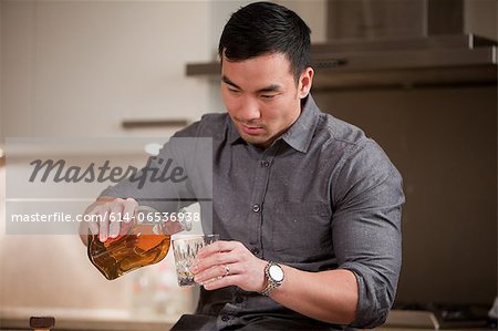 Man pouring glass of whiskey in kitchen