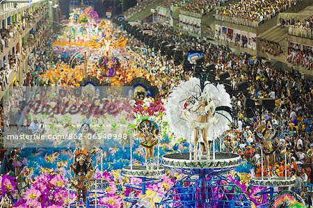 South America, Rio de Janeiro, Rio de Janeiro city, costumed dancer in a feather headdress and the floats and dancers of the Caprichosos samba school at carnival in the Sambadrome Marques de Sapucai