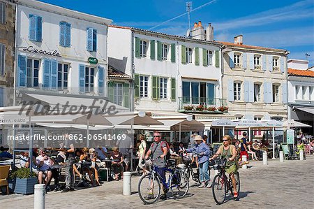 France, Charente Maritime, Ile de Re.  Tourists eat at tables set outside the cafes and restaurants that overlook the small harbour in La Flotte.