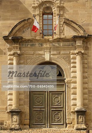 ornate facade with France flags, pillars, and wooden door on Porterie de l'abbaye in the small medieval village of Saint-Antoine-l'Abbaye, France