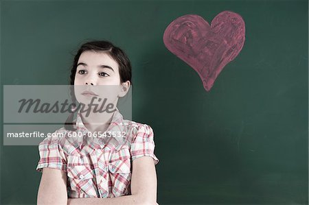 Portrait of Girl with Arms Crossed and Looking to the Side in front of Chalkboard with Heart Drawing in Classroom
