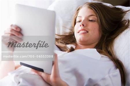 Woman lying on bed in her bedroom using digital tablet computer