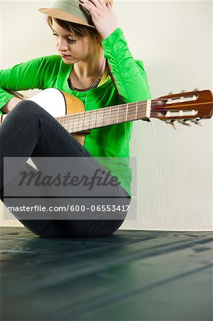 Portrait of Teenage Girl Sitting on Floor, Wearing Hat and holding Acoustic Guitar, Studio Shot on White Background