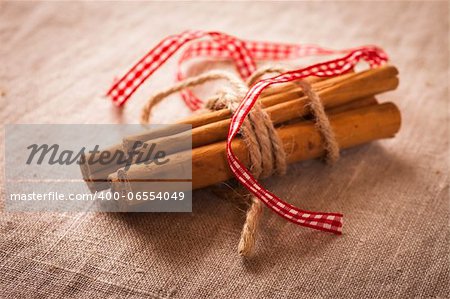 Decorative, sparse christmas arrangement with greeting card copyspace for "Merry Christmas"-text. Cinnamon sticks with one brown and one red ribbon around on a brown canvas table cloth.