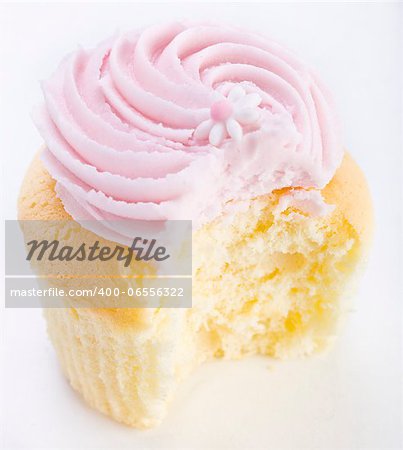 Pink frosted cupcake with flower decoration and a bite missing