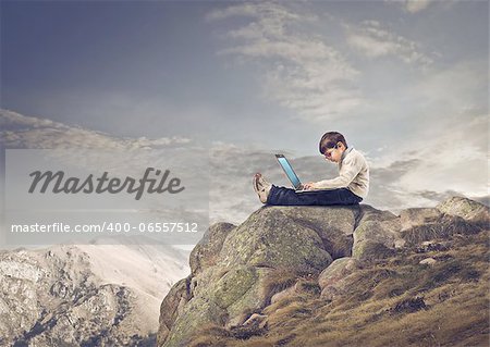Child using a laptop sitting on a rock