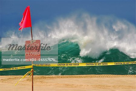 A large swell from the northwest creates very dangerous conditions at Waimea Bay on Oahu in Hawaii. Here is a 'beach closed' sign on the beach with massive shore break in the background.