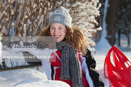 Blond teenager girl sitting on a bench in a snowy park