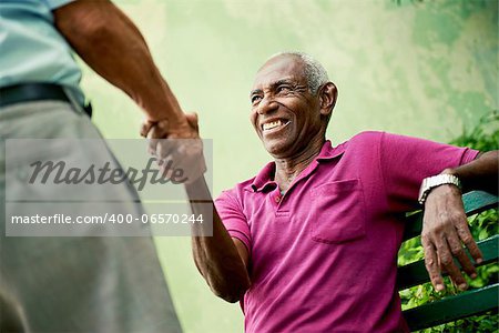 retired elderly people and free time, happy senior african american and caucasian male friends greeting and sitting on bench in park