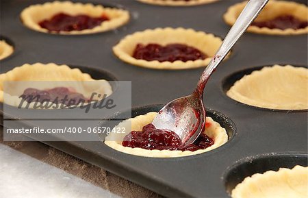 Closeup of jam tarts being filled with a metal teaspoon