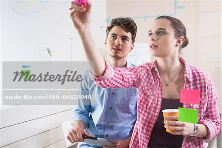 Young Man and Young Woman Working in an Office, Looking Through Glass Board, Germany