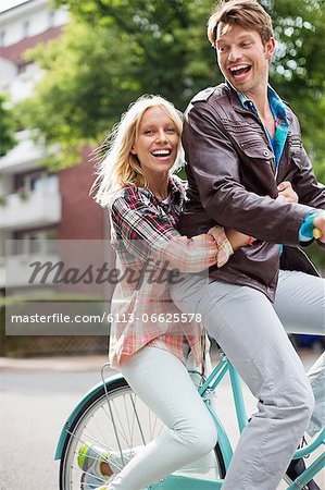 Couple riding bicycle together on city street