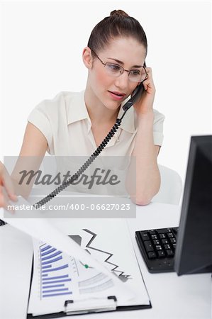 Portrait of a saleswoman making a phone call while looking at statistics against a white background