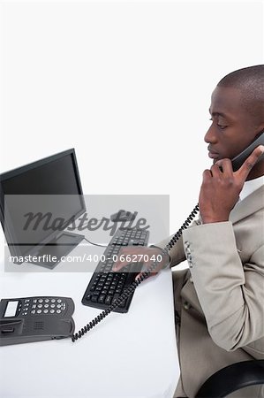 Side view of a secretary answering the phone while using a computer against a white background