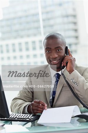 Portrait of a smiling entrepreneur making a phone call while reading a document in his office