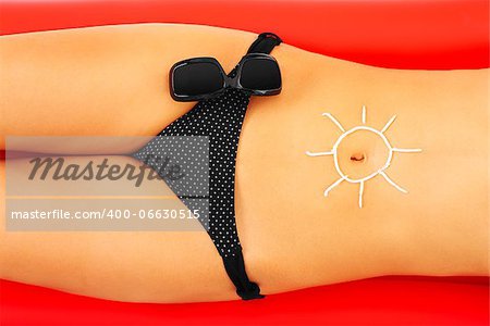 A picture of a sexy woman with a sun symbol on belly made of sunscreen on a red mattress