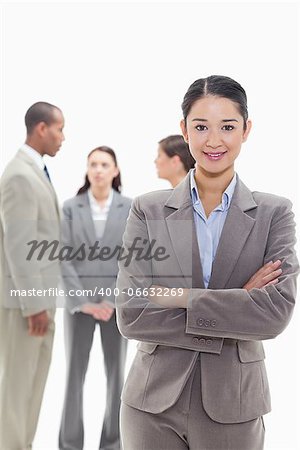 Businesswoman smiling and crossing her arms with co-workers talking in the background