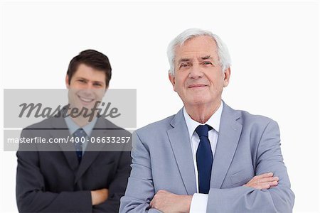 Close up of mature businessman with folded arms and colleague behind him against a white background