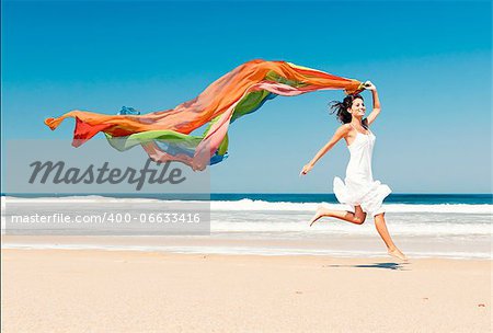 Beautiful girl in the beach running and holding a colored piece of fabric