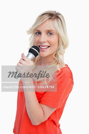 Young attractive and blonde woman smiling while singing in a cordless microphone