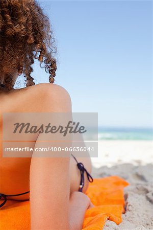 Back view of a young woman lying on her orange beach towel in front of the sea