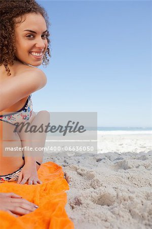 Young smiling woman turning her head back while sitting in front of the sea